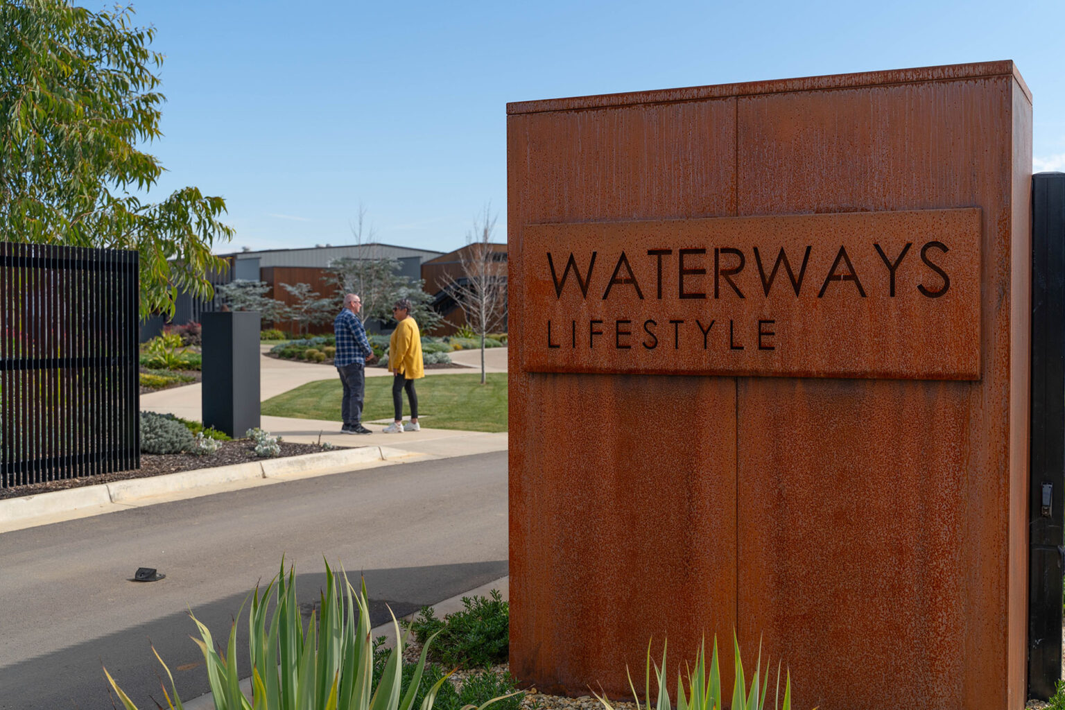 People talking in background behind entry statement at Waterways Lifestyle Village.