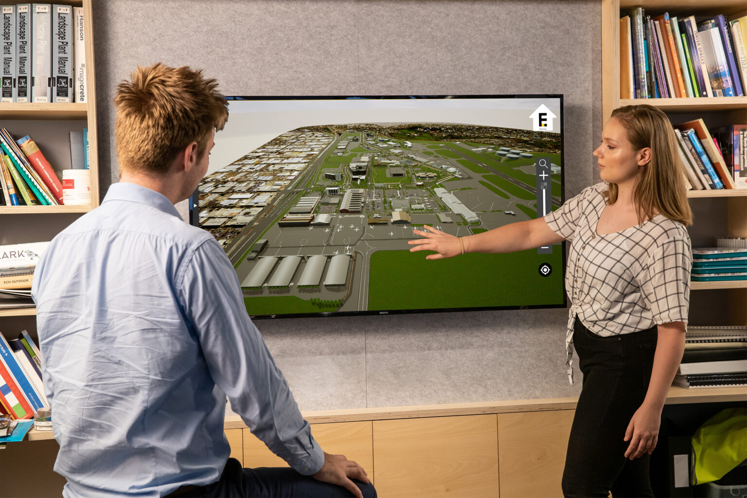 A man and woman view a large screen featuring the 3D model of the Essendon Fields Interactive Display project.